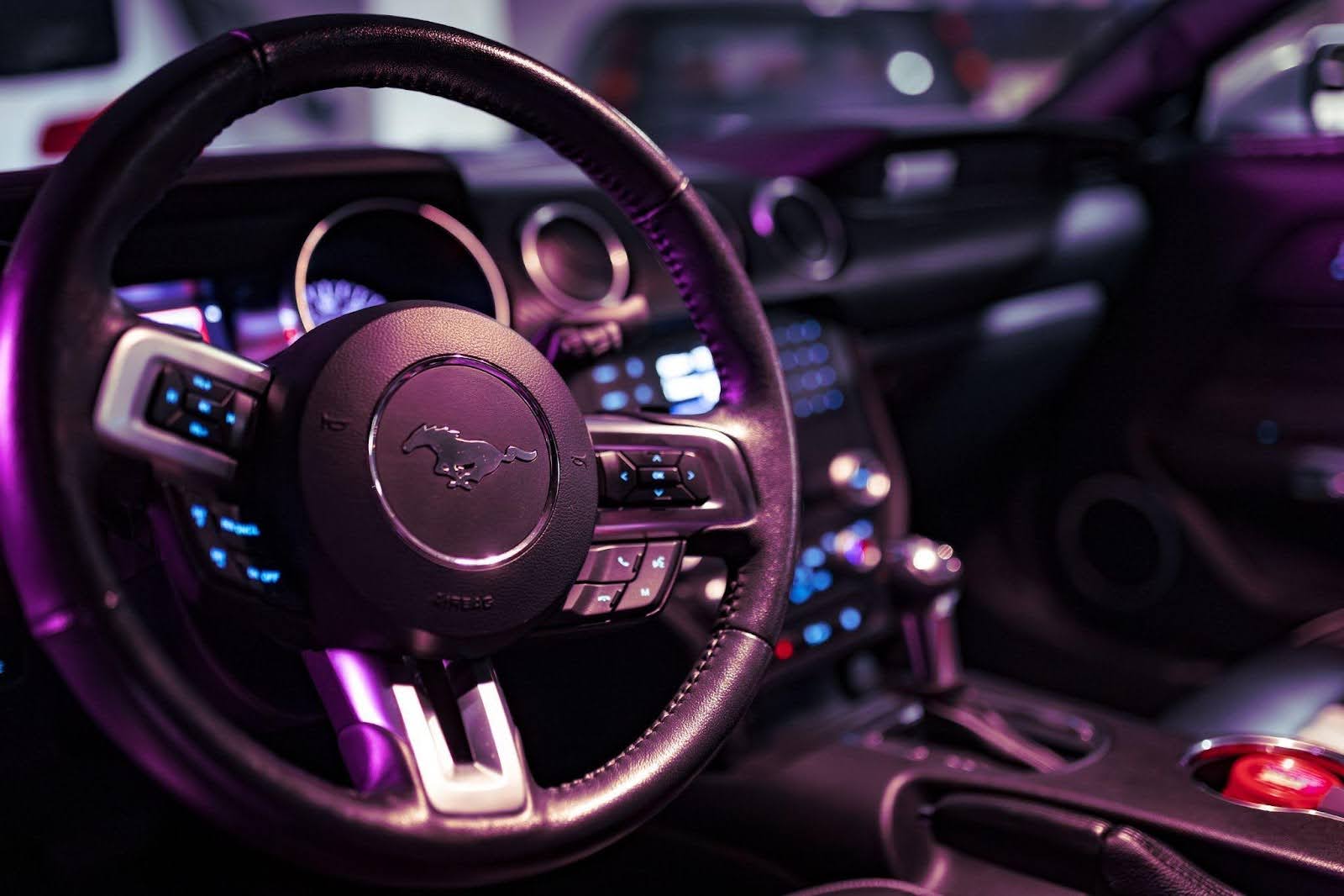 A sleek car bathed in purple light showcasing its steering wheel prominently