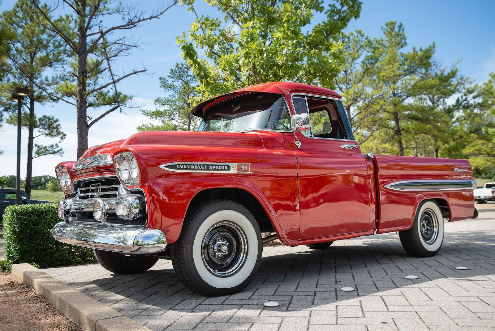 Classic red Chevrolet Apache 31 Fleetside truck parked on a paved area with trees in the background.