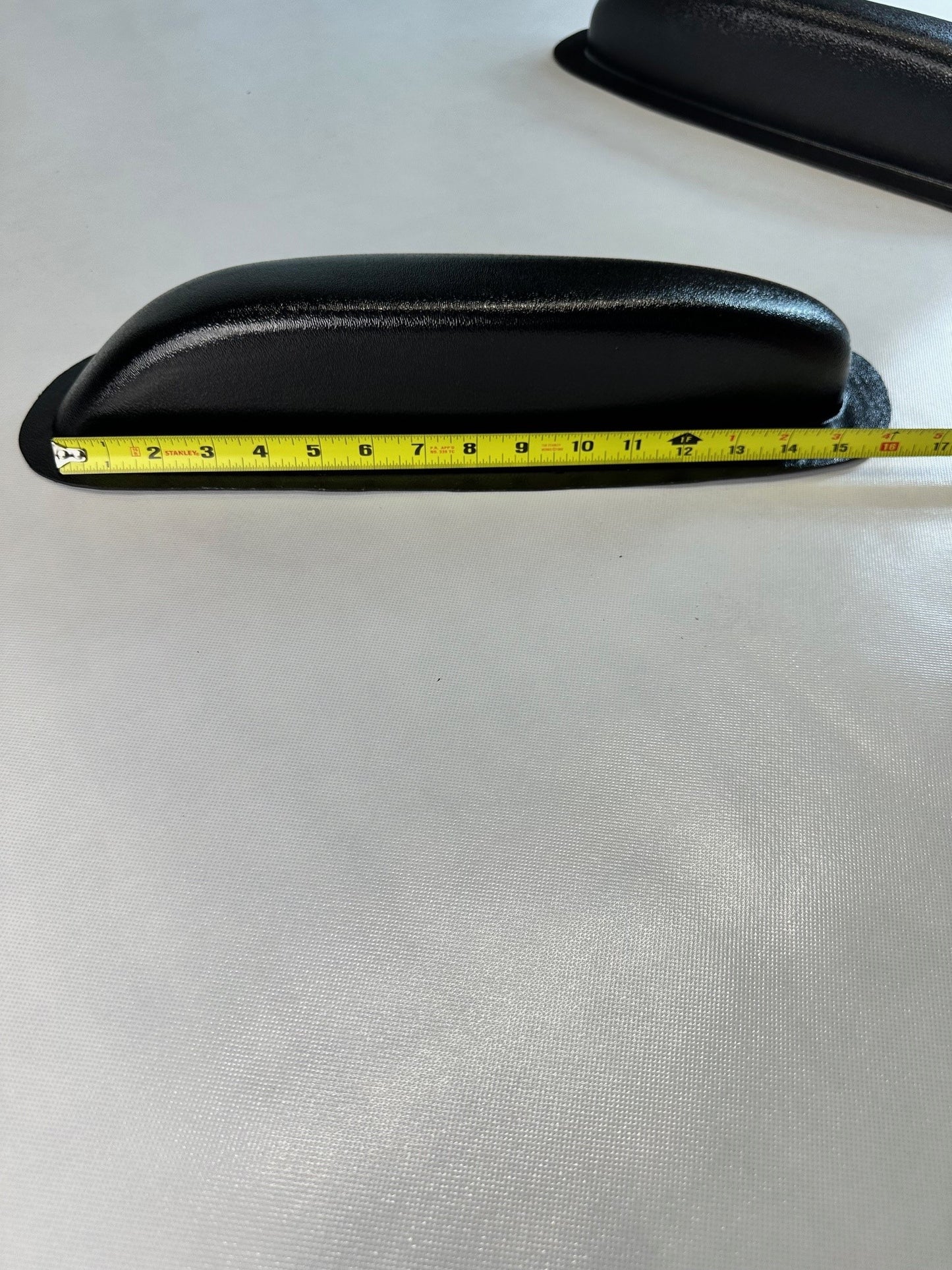 Black car door handle with a measuring tape for scale on a light gray background