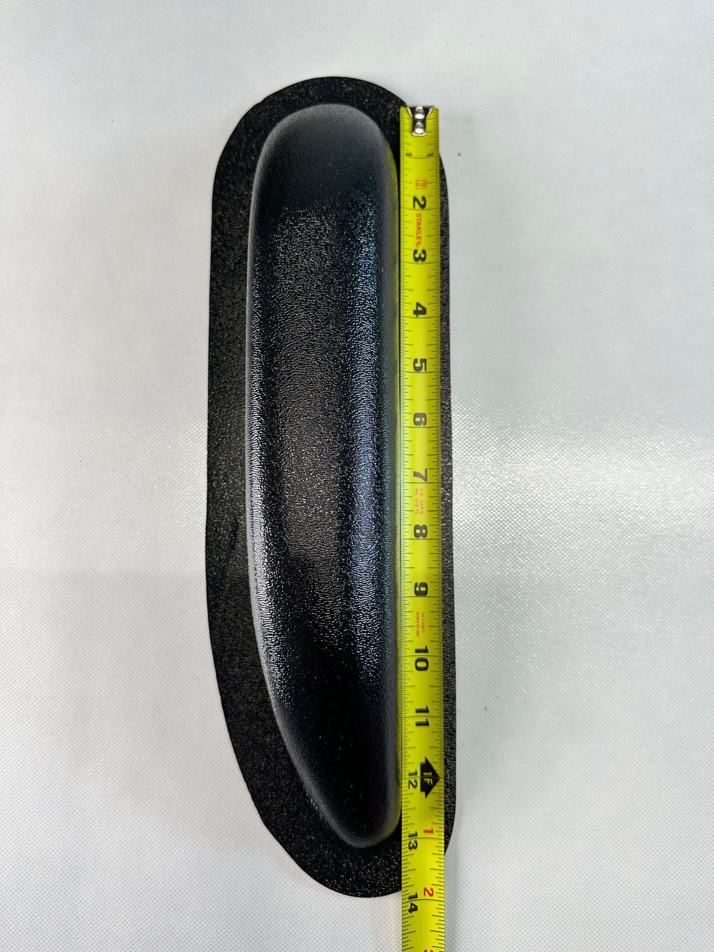 Black oval object with a tape measure for scale on a white background