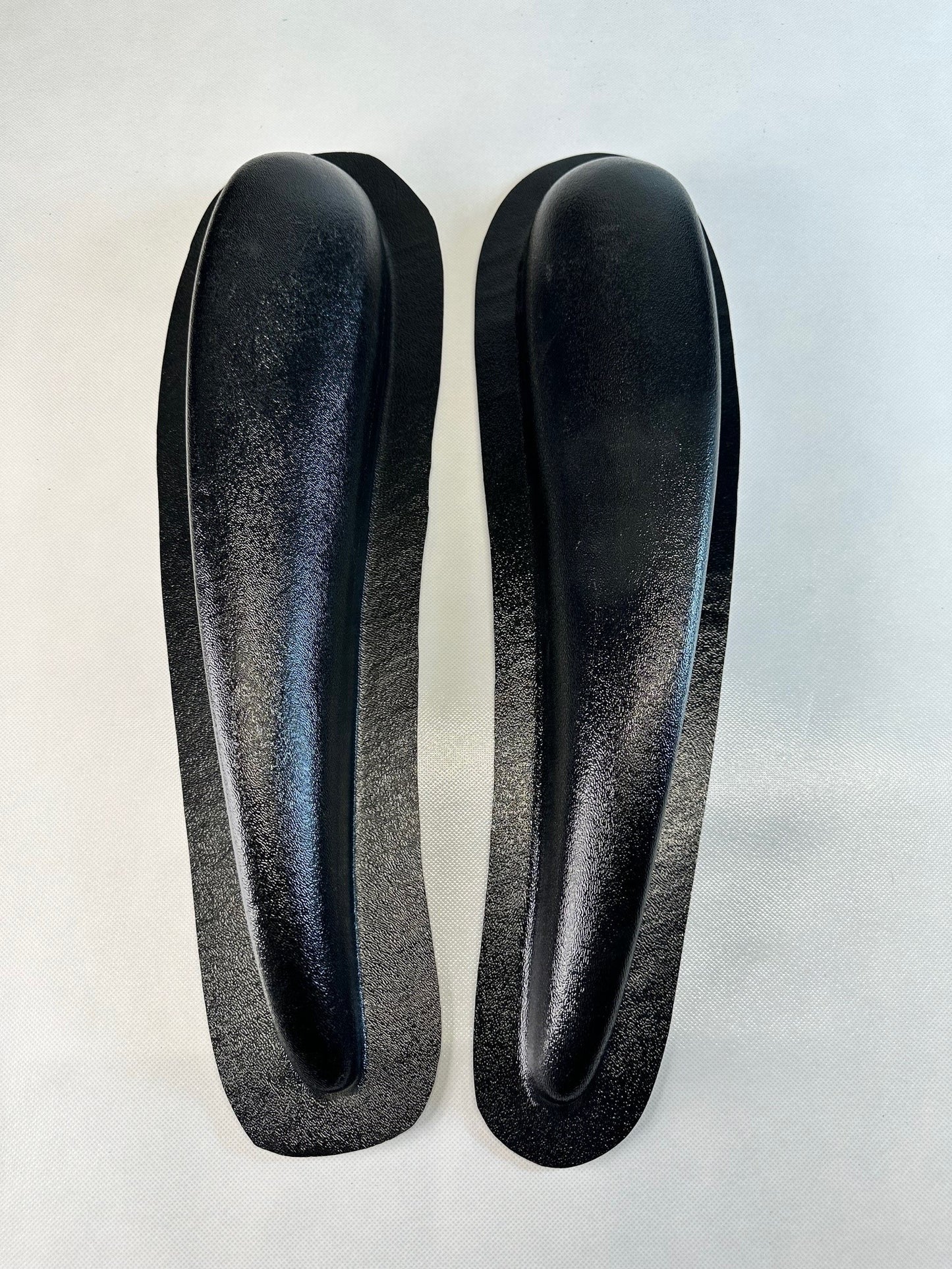 Two black shoe inserts on a light gray background