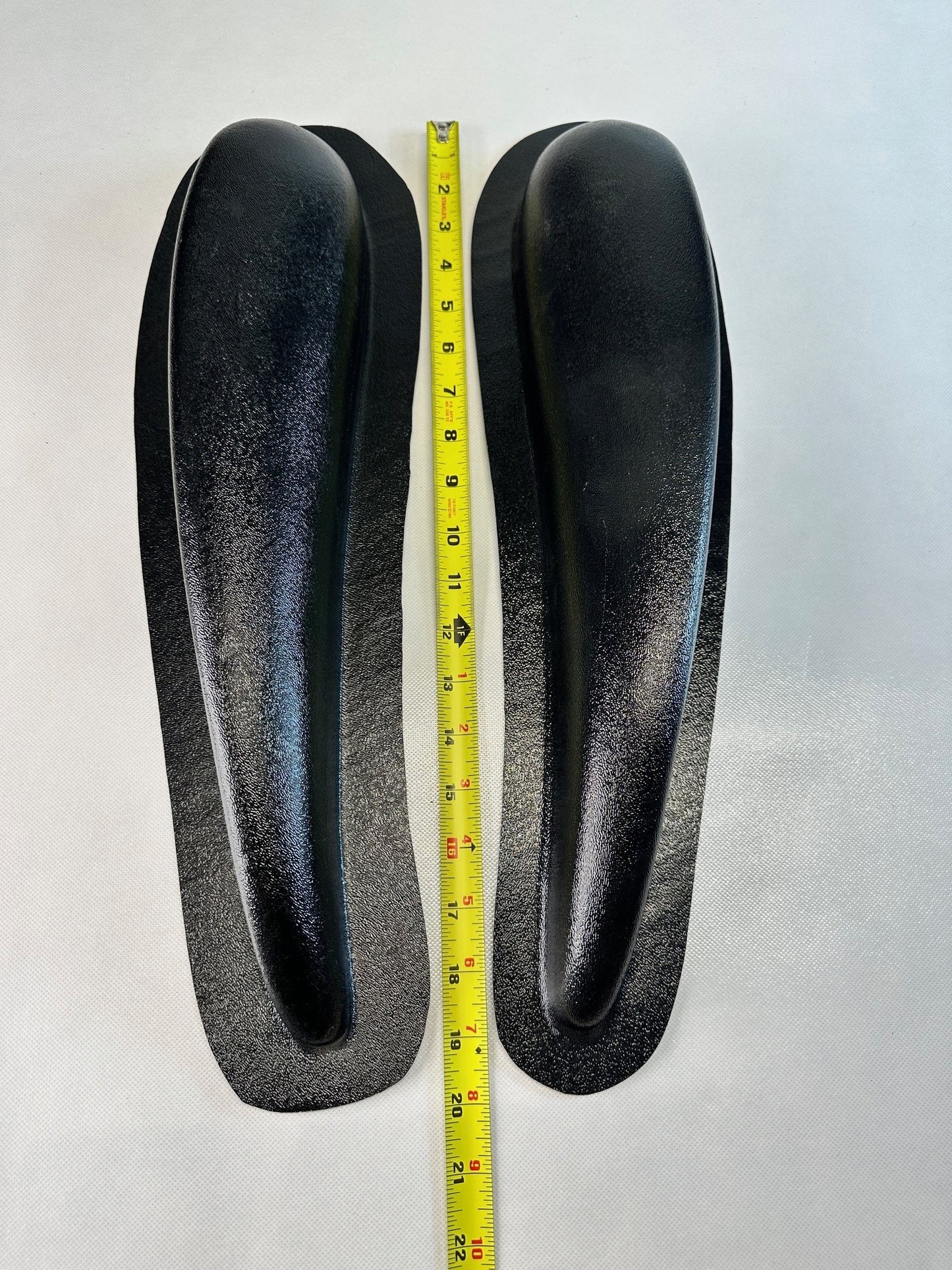Two black shoe inserts with a measuring tape between them on a light gray background