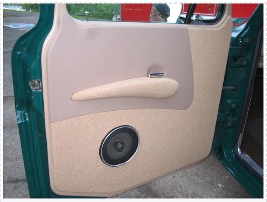 Car door panel with beige interior and a speaker, showing signs of wear.