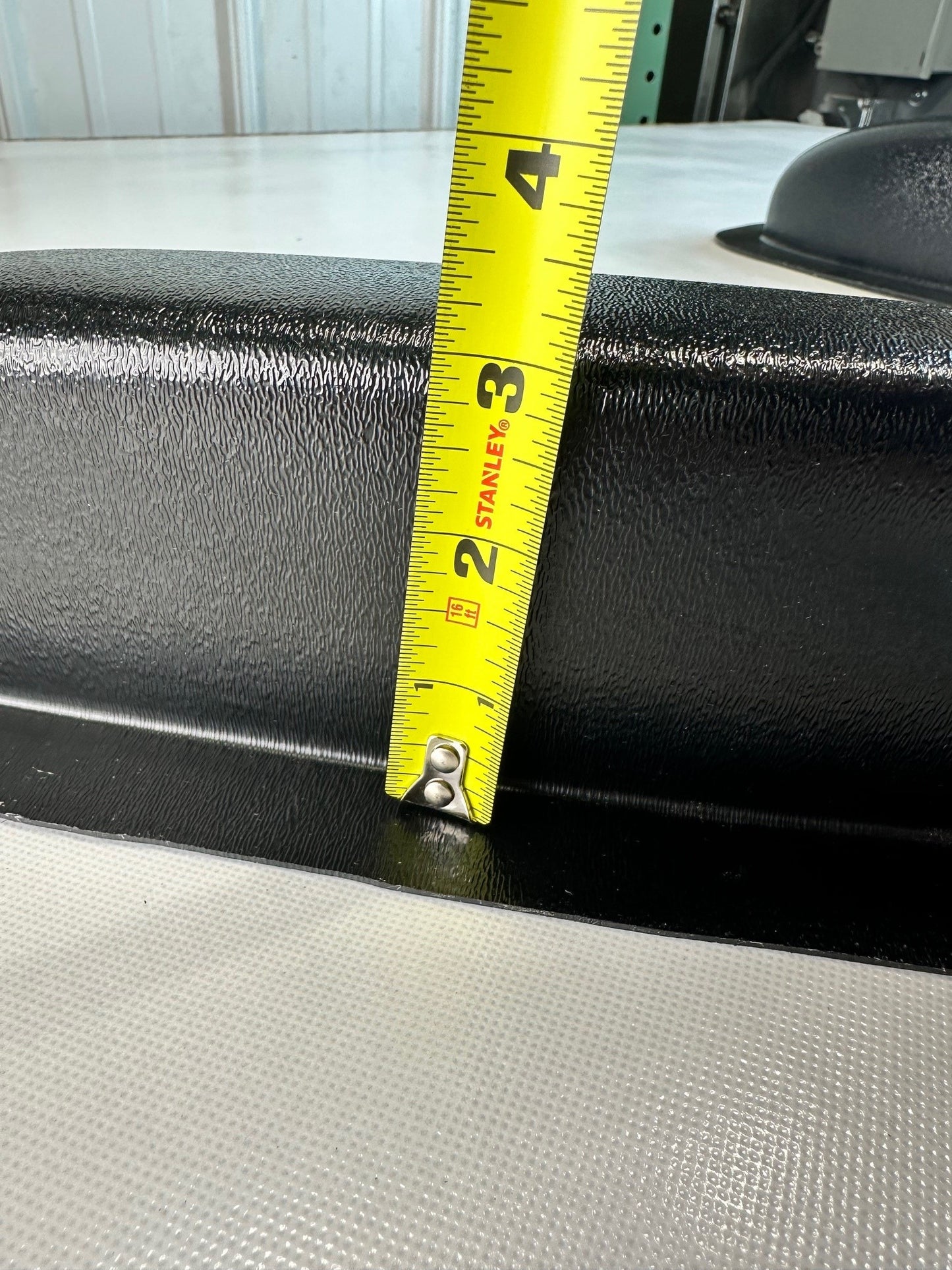 Black universal modular ABS armrest showing height of armrest with a tape measure