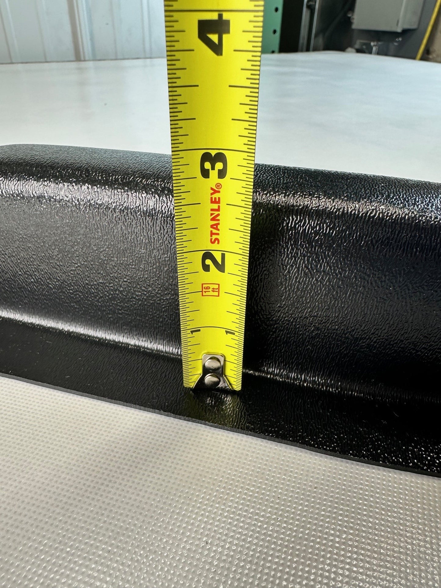 Close-up of black ABS universal modular armrest edge with measuring tape indicating protrusion depth
