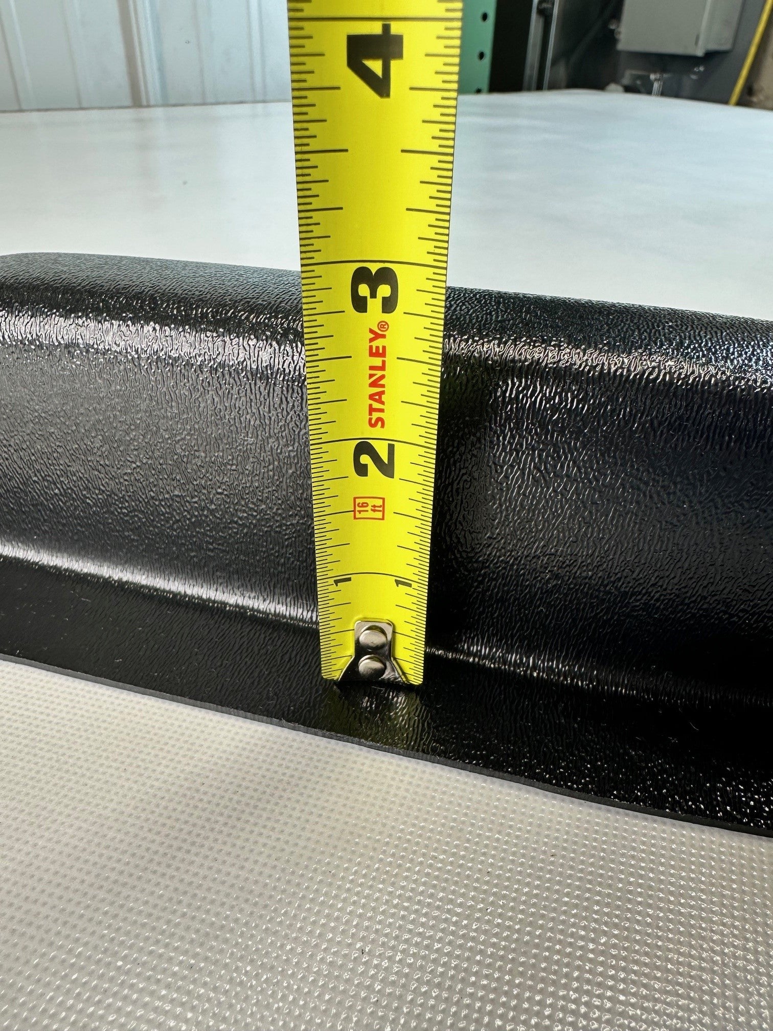 Close-up of black ABS universal modular armrest edge with measuring tape indicating protrusion depth