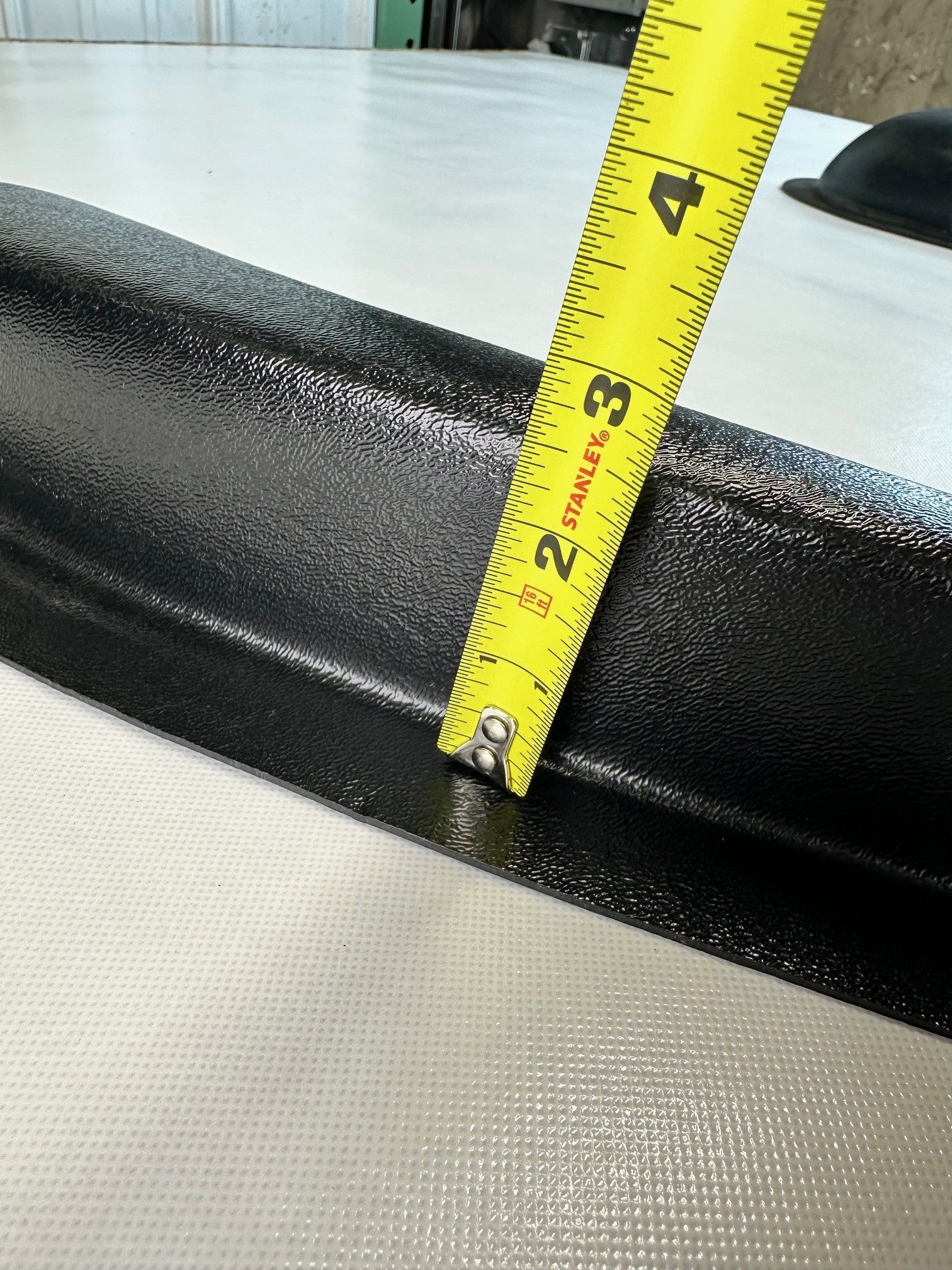 Close-up of black ABS universal modular armrest edge with measuring tape indicating protrusion depth
