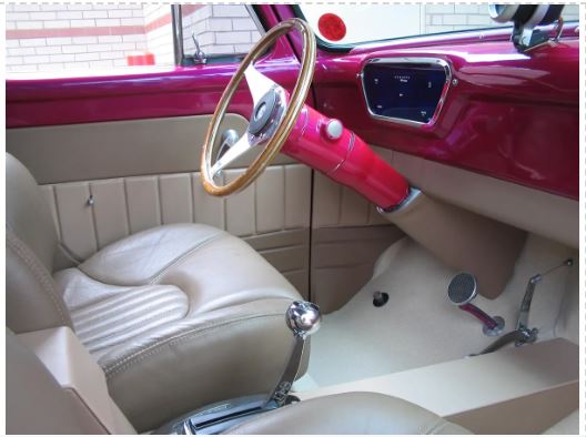 Interior view of a vehicle featuring a red under dash cover kit with a white seat and a wooden steering wheel.