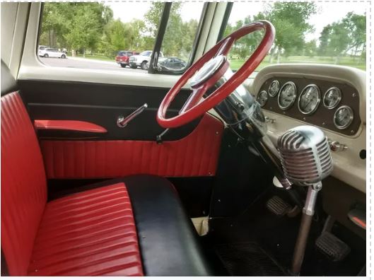 Interior view of a vintage Ford truck with red door panels and black leather seats, featuring a wood steering wheel and analog instrument panel.