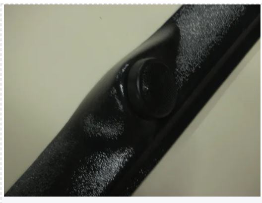 Close-up of a black metal rod with a textured surface on a light background