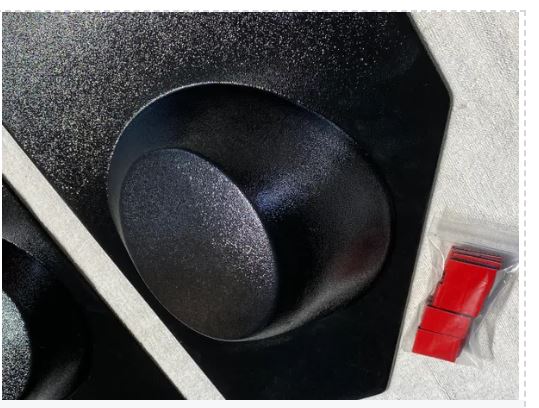 Close-up of a black speaker cone with a red component in the background