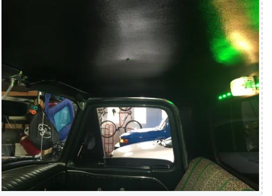 View from inside a vehicle looking out through a rearview mirror at a street scene with parked cars.