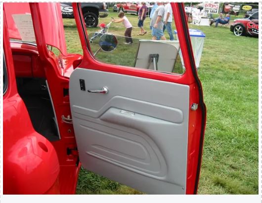 Red car door with white interior on a grassy outdoor setting