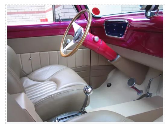 Close-up of a classic car's interior with a pink dashboard and beige seats.