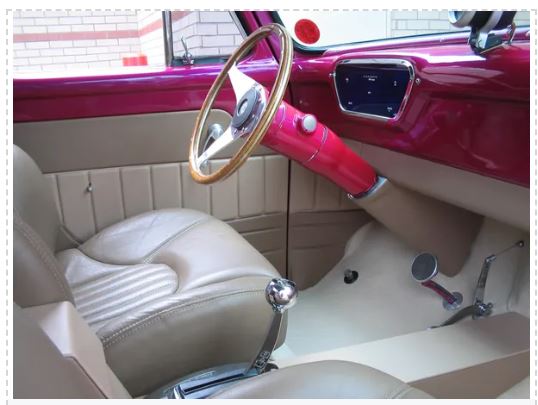 Close-up of a vintage car's interior with a pink dashboard and beige seats.