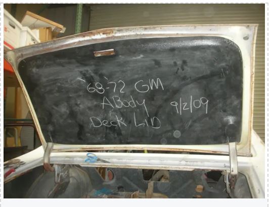 A used 1955-1957 Chevrolet deck lid cover with writing on it, placed against a white background.