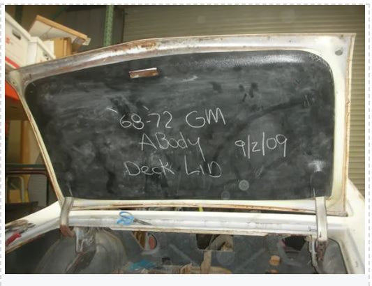 A used 1955-1957 Chevrolet deck lid cover with writing on it, placed against a white background.