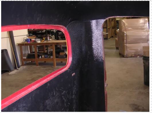 Rear cab cover of a vehicle, primarily black with a red trim, showing the interior of the vehicle in the background.